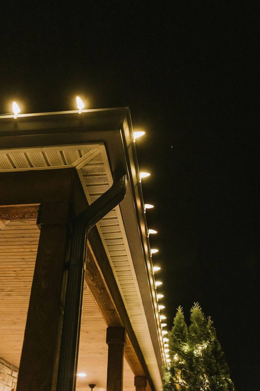 Close-up of evenly spaced warm white C9 bulbs clipped along a home's gutter line and roof peak at night