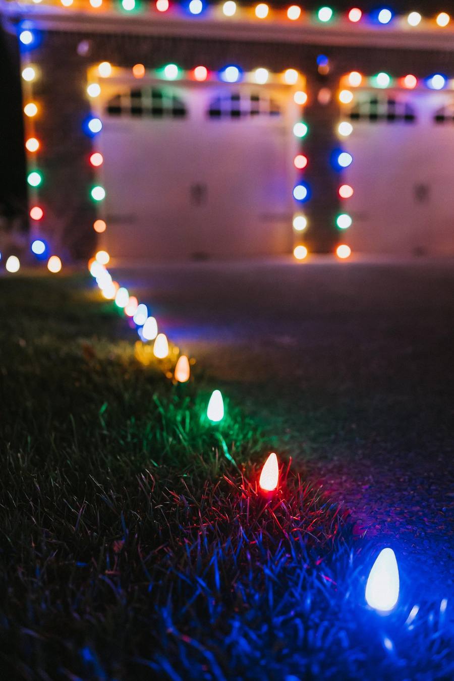 Close-up of multicolor C9 pathway lights staked along a walkway leading to a lit garage