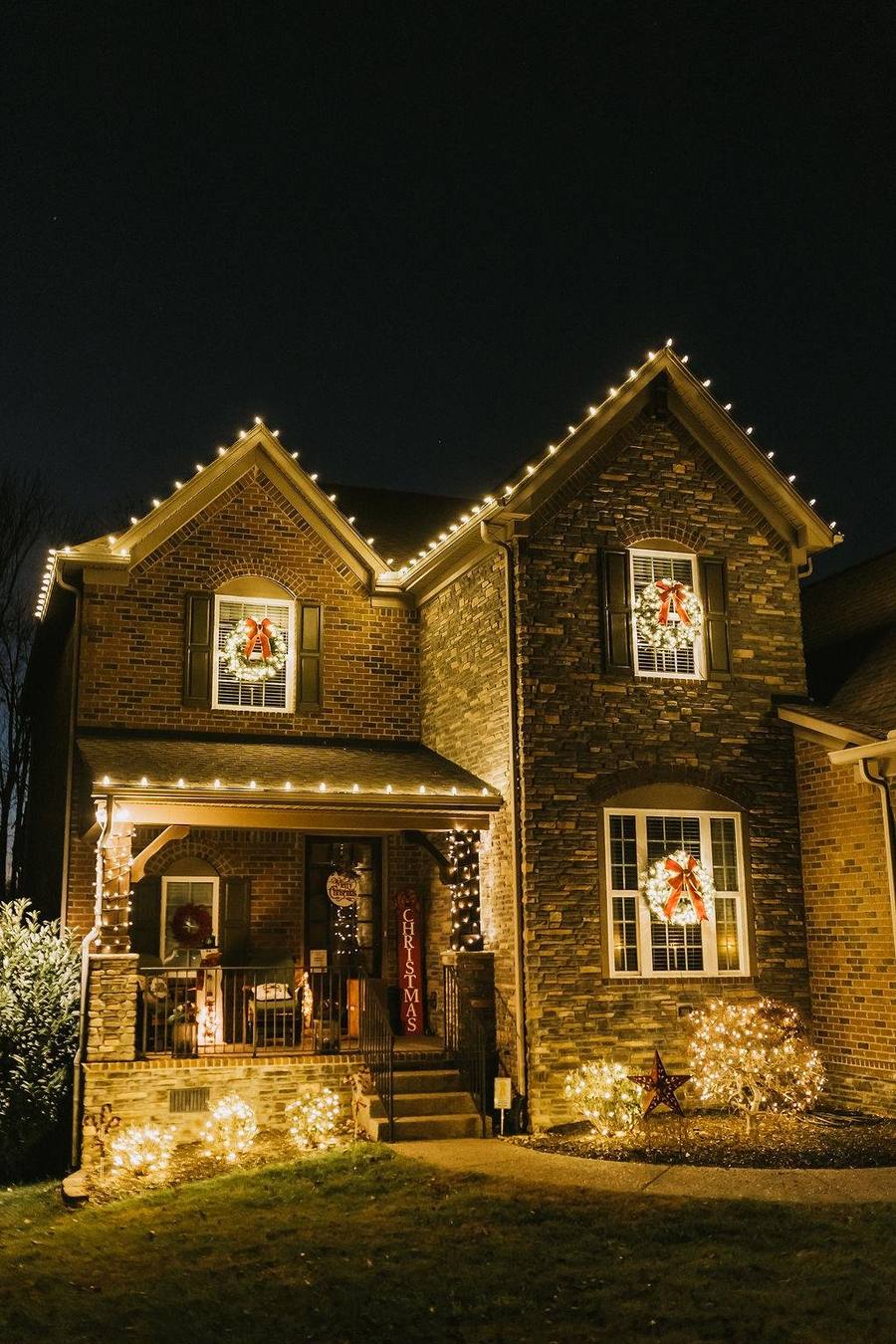 Two-story brick home in Bentonville outlined in warm white lights with lit wreaths and red bows in every window